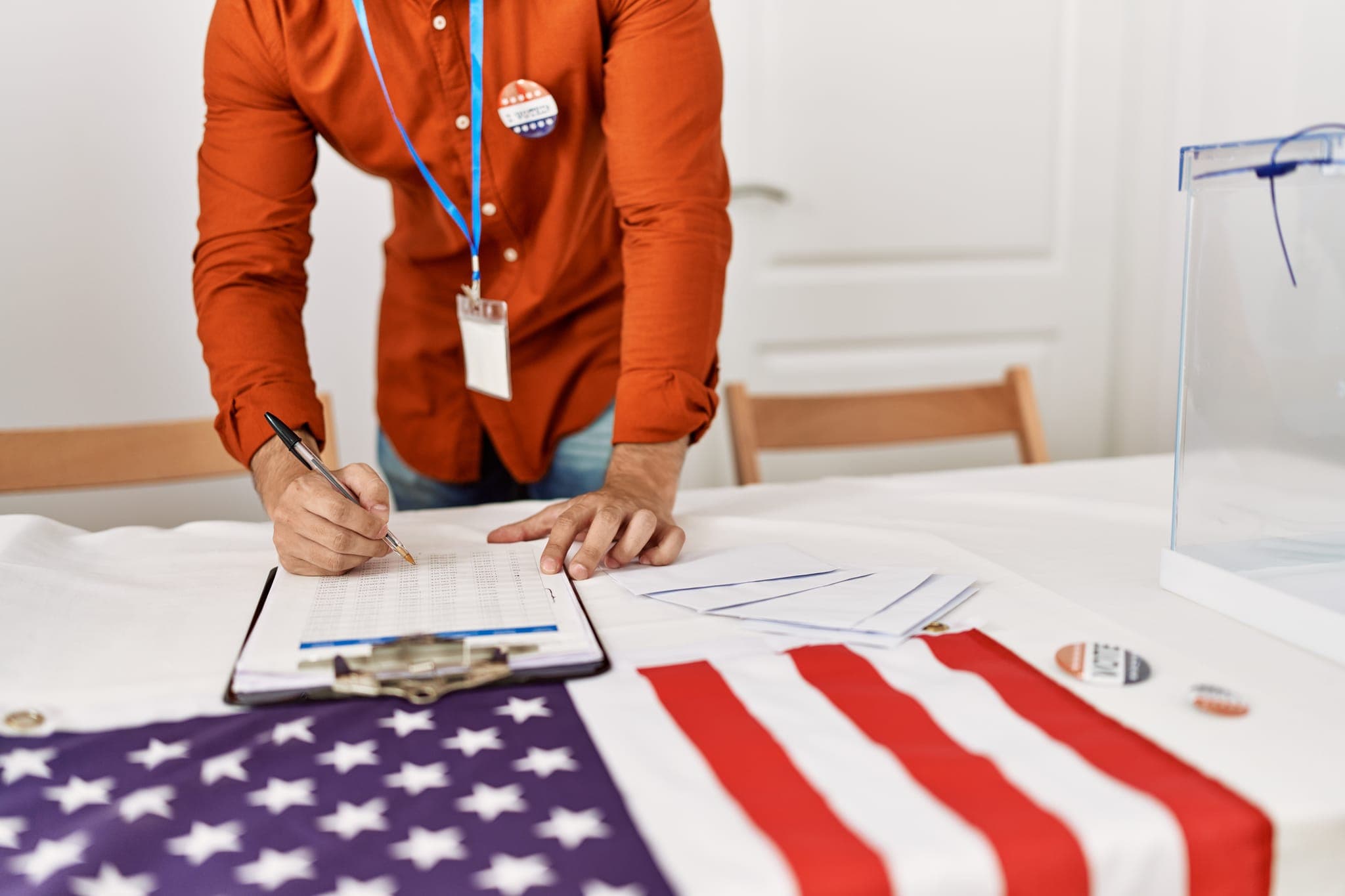 Election worker completing voter registration paperwork beside an American flag